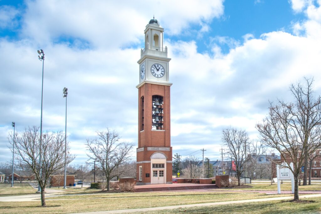 Large brick clock tower in the middle of a field, a sign that reads, "pulley Tower"